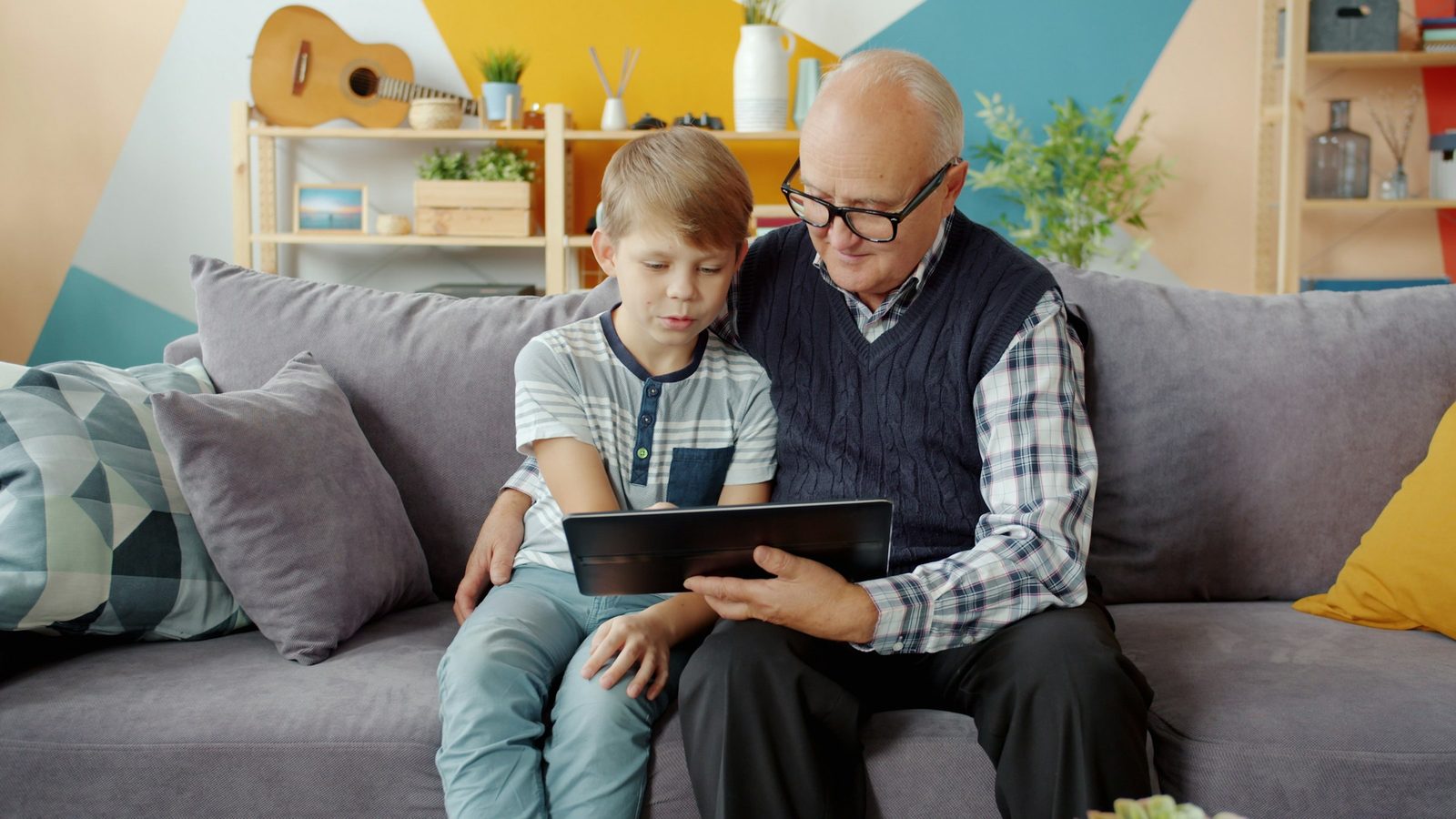 Ein Grossvater und sein Enkel sitzen auf dem Sofa und schauen gemeinsam auf ein Tablet.